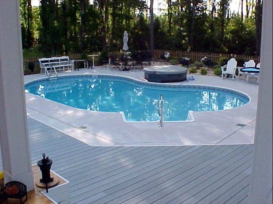 Grey composite deck wrapping around a backyard swimming pool