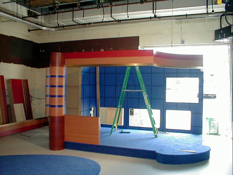 Television news set under construction with blue panels and a curved anchor desk